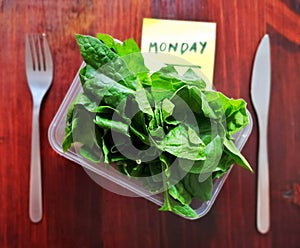 Monday meal concept. Tupperware with spinach leaves.