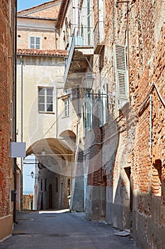 Old street with red bricks buildings and arch in a summer day, nobody in Mondovi, Italy