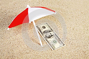 Money american hundred dollar bill unter sunshade on beach sand