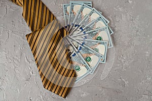 money of American one hundred dollars lie fan with mens yellow black striped tie on gray concrete background