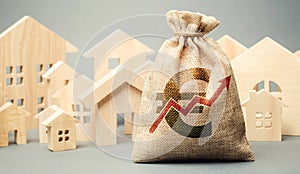 Money bag with arrow up and miniature wooden houses. The concept of rising property prices. High mortgage rates. Expensive rental