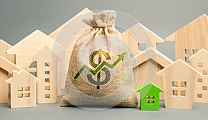 Money bag with arrow up and miniature wooden houses. The concept of rising property prices. High mortgage rates. Expensive rental