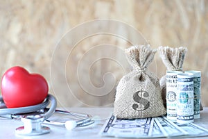 Money bag with banknote and stethoscope with red heart on wooden