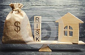 Money bag, blocks with the word Risk and a wooden house on the scales. The concept of losing money when investing in real estate.