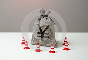 Money bag with chinese yuan or japanese yen symbol blocked by road cones. National money reserve. Freezing of accounts and