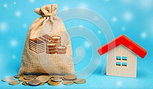 Money bag with coins and a wooden house with snow. Real estate market in the winter season. Christmas sale / discounts concept.