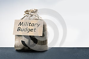 money bag, dollar sign, military budget text on grey background with copy space