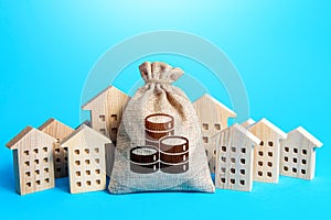 Money bag among town houses figurines. Municipal budgeting. Rich city. Rental business. Realtor services. Sale of real estate.