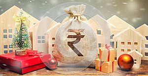 Money bag, wooden houses, Christmas tree and gifts. Christmas Sale of Real Estate. New Year discounts for buying housing. Purchase