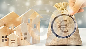 Money bag and a wooden houses with snow. Conceptual image real estate market in the winter season. Christmas sale / discounts