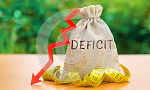 Money bag with the word Deficit and tape measure with down arrow. Budget deficit concept. Low profit. Financial costs. Bankruptcy