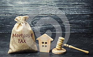 Money bag with the word Mortgage tax, judge`s hammer and wooden house. Mortgage credit lending. Tax refund when buying an