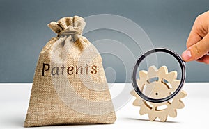 Money bag with the word Patents and a wooden gear. Registration of patents and copyright compliance. Licensing technology and