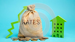 Money bag with the word Rates, up arrow and wooden house. The concept of a high mortgage loan rate. Buy and rental. Expensive