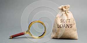 Money bag with the word Soft loans and a magnifying glass. Loan with a below-market rate of interest soft financing. State