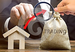 A money bag with the word Trading, an up arrow and a wooden house. The concept of increasing the demand for home purchase. Supply