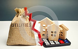 Money bag with the word Utilities and an arrow down and wooden houses on the calculator. Reduced prices for utilities. Low prices photo