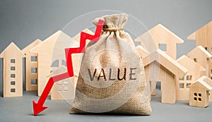 A money bag with the word Value, wooden houses and down arrow. The concept of reducing the market prices of real estate. Low price