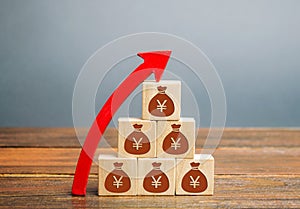Money bags with yuan symbol on wooden blocks and up arrow. The concept of a successful business. Increase profits and capital.