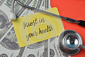 Money banknotes, stethoscope and yellow card with text INVEST IN YOUR HEALTH