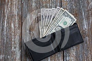 Money in the black leather wallet lying on rustic wooden background. Dollars for making purchases and byung things. Shopping time