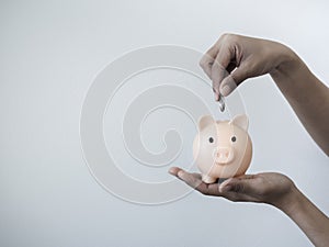 Money box on hand. Hand puts coin into the pink piggy bank on hand white background.