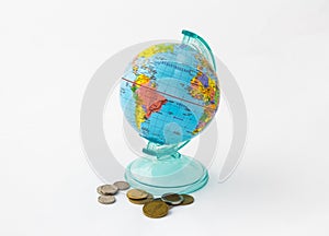 A money box made in the form of a globe, the planet Earth with a money slot at the top stands near to several coins, on a