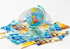 A money box made in the form of a globe, the planet Earth with a money slot at the top stands on a stack of Israeli banknotes of d