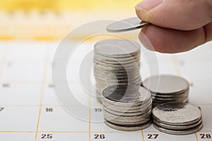 Money Business Saving and Planning Concept. Closeup of man finger holding coin and put to top of stack of coins on calendar