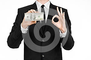 Money and business theme: a man in a black suit holding a bill of 100 dollars and features a hand gesture on an isolated white bac