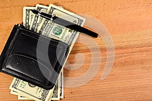 Money clip and one hundred dollars banknotes on wooden table