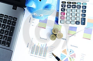 Money coins stack and business fountain pen and calculator and eyeglasses and blue piggy bank labtop with document chart on desk