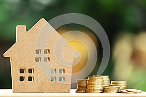 Money coins stacked on each other in different positions and home in brown recycled paper model on the wooden table. Credit financ