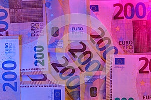 Money colored background. Two hundred euro bills close-up in purple neon light.Euro exchange rate in the European Union