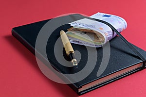 money counting. Accounting black book, euro banknotes and fountain pen on red background
