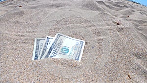 Money dolars half covered with sand lie on beach close-up.