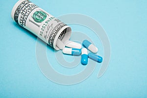 Money dollar rolled up with pills flowing out  on blue background, high costs of expensive medication concept. Copy space