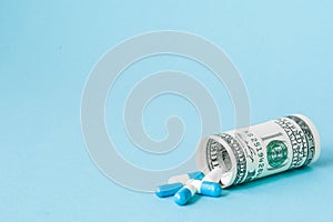 Money dollar rolled up with pills flowing out  on blue background, high costs of expensive medication concept. Copy space