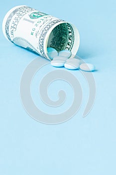 Money dollar rolled up with pills flowing out  on blue background, high costs of expensive medication concept. Copy space