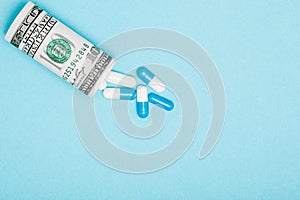 Money dollar rolled up with pills flowing out isolated on blue background, high costs of expensive medication concept. Copy space