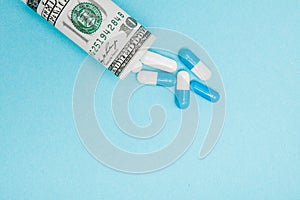 Money dollar rolled up with pills flowing out isolated on blue background, high costs of expensive medication concept. Copy space