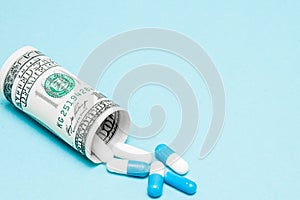 Money dollar rolled up with pills flowing out isolated on blue background, high costs of expensive medication concept. Copy space