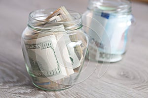 Money. Dollars and euro in two open jars on grey wooden background. Copy space.