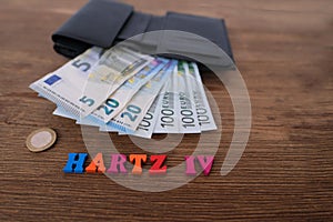 Money, euro banknotes, black wallet, word in German Hartz IV made of colored letters lie on old wooden table, concept of social
