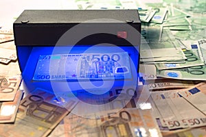 Money fake testing - euro banknotes authentication check in UV Currency Detector lights. Counterfeiting banknotes, checking at the