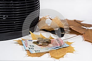 Money for heating bills with black heater on white background. Autumn season