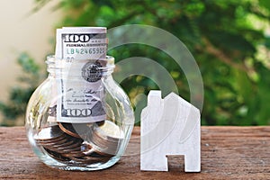 Money for housing. Wooden house model, Coins and banknote in glass jar with greenery background