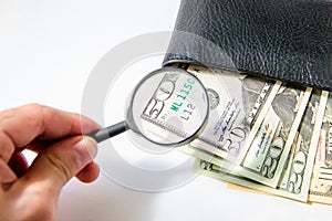 Money, hundred american dollars under a magnifying glass in black leather purse on white background