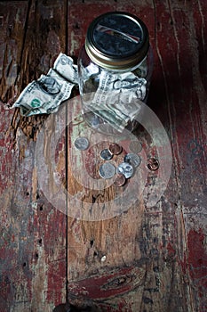 Money jar with dollars and change on old wooden table