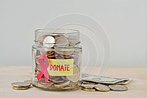 Money jar full of coins with pink ribbon and Donate label - Breast cancer charity and research fund concept